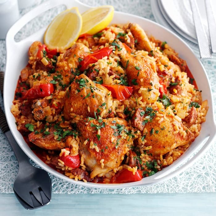 Chicken and rice in a serving bowl with roasted pepper, lemon, and parsley