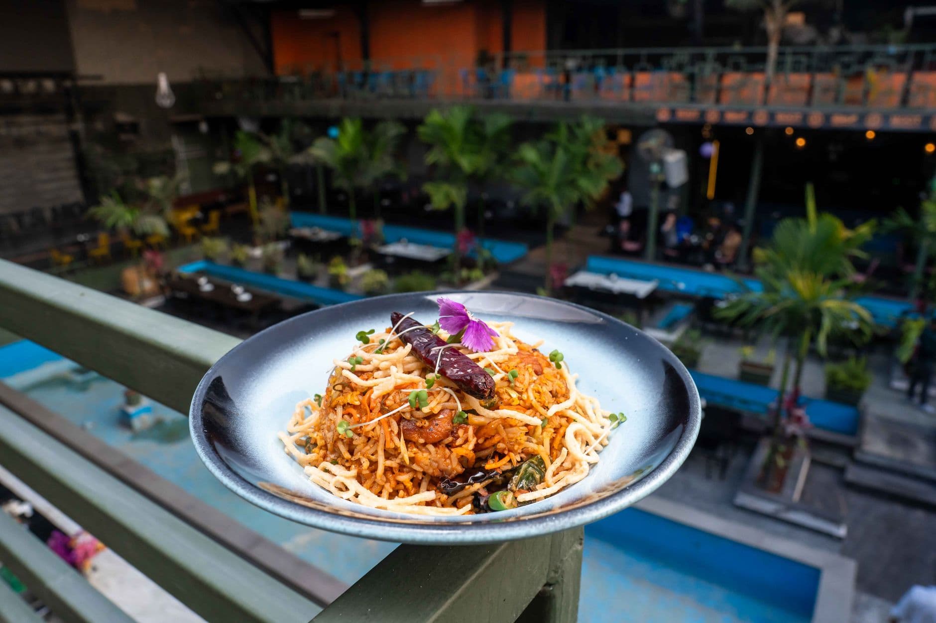 A plate of Asian chicken fried rice garnished with herbs and flowers, served outdoors.
