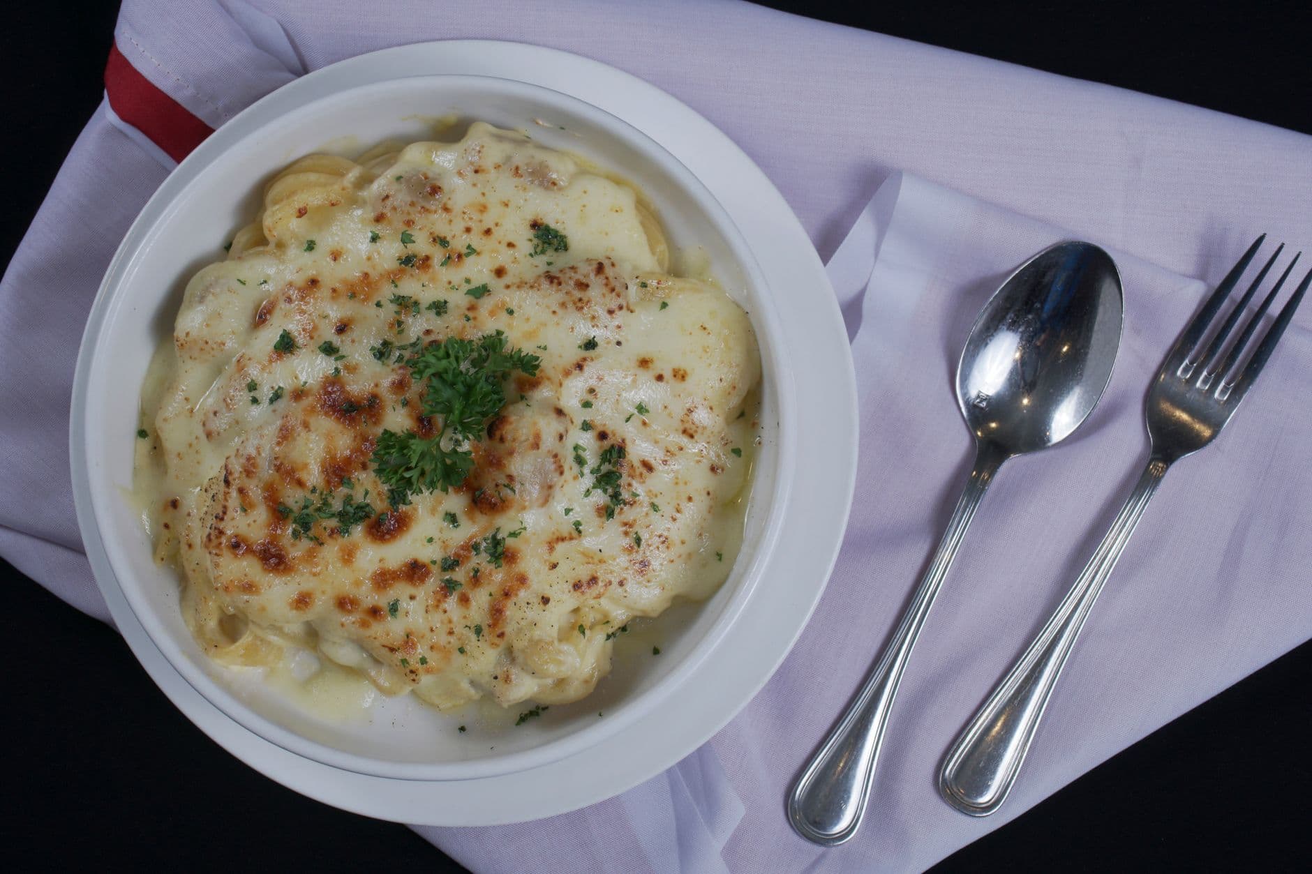 Delicious creamy baked pasta topped with parsley and served on a white napkin.